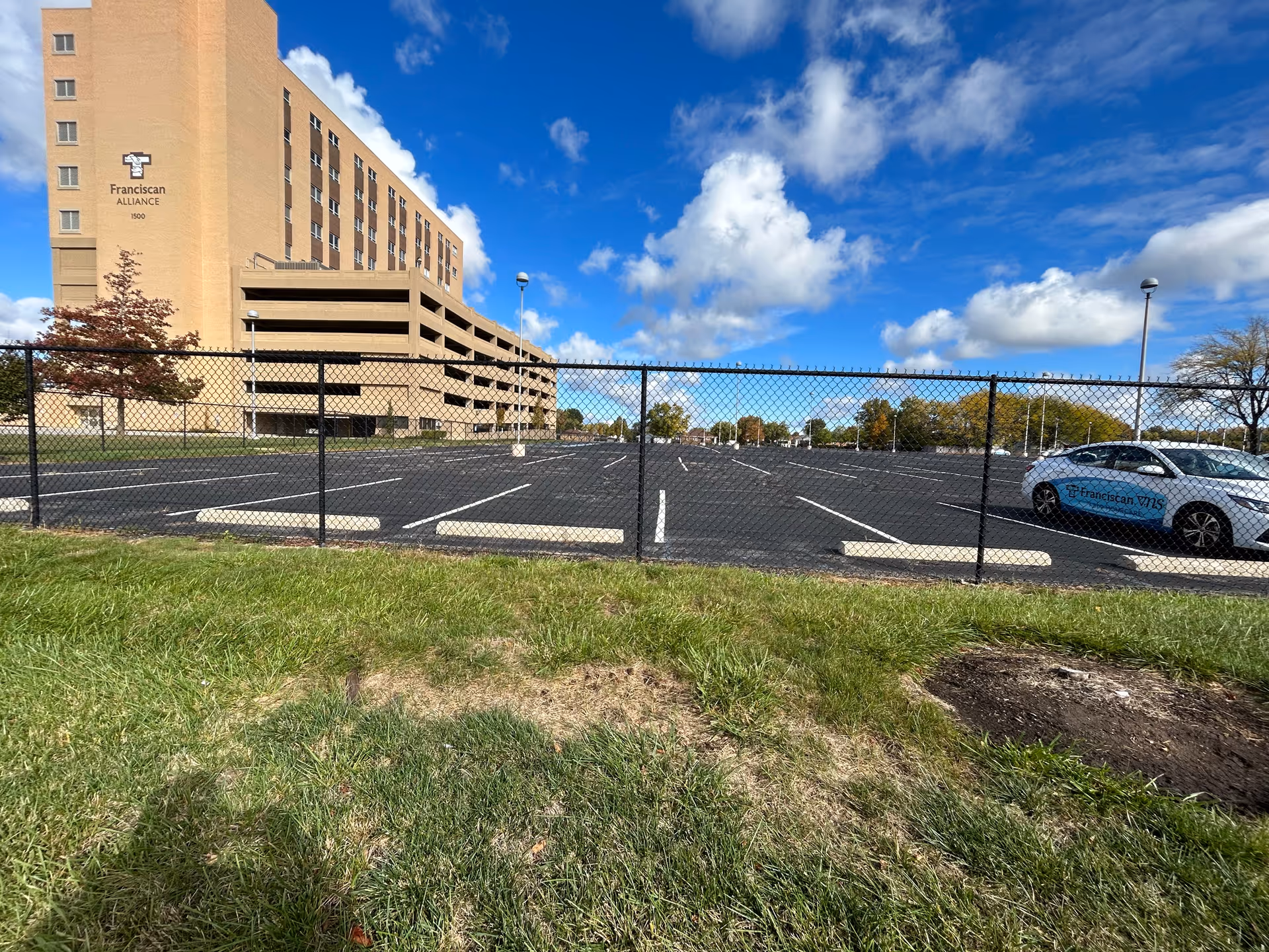 Exterior view of a beige senior living building with a parking lot behind a chain-link fence.