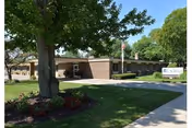 Exterior view of Laurels of Hudsonville with brick entrance, sign, trees, and lawn.