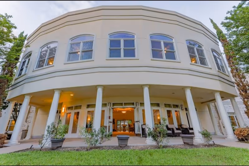 Curved cream-colored senior living facility facade with columns and glass doors.