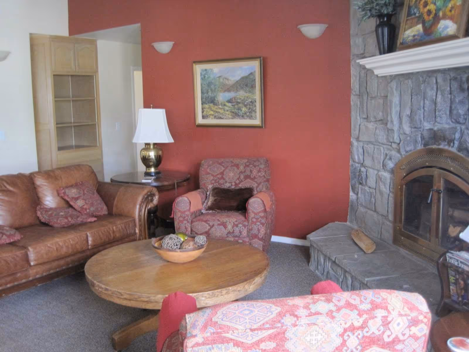 Cozy living room with a red wall, stone fireplace, and leather seating.
