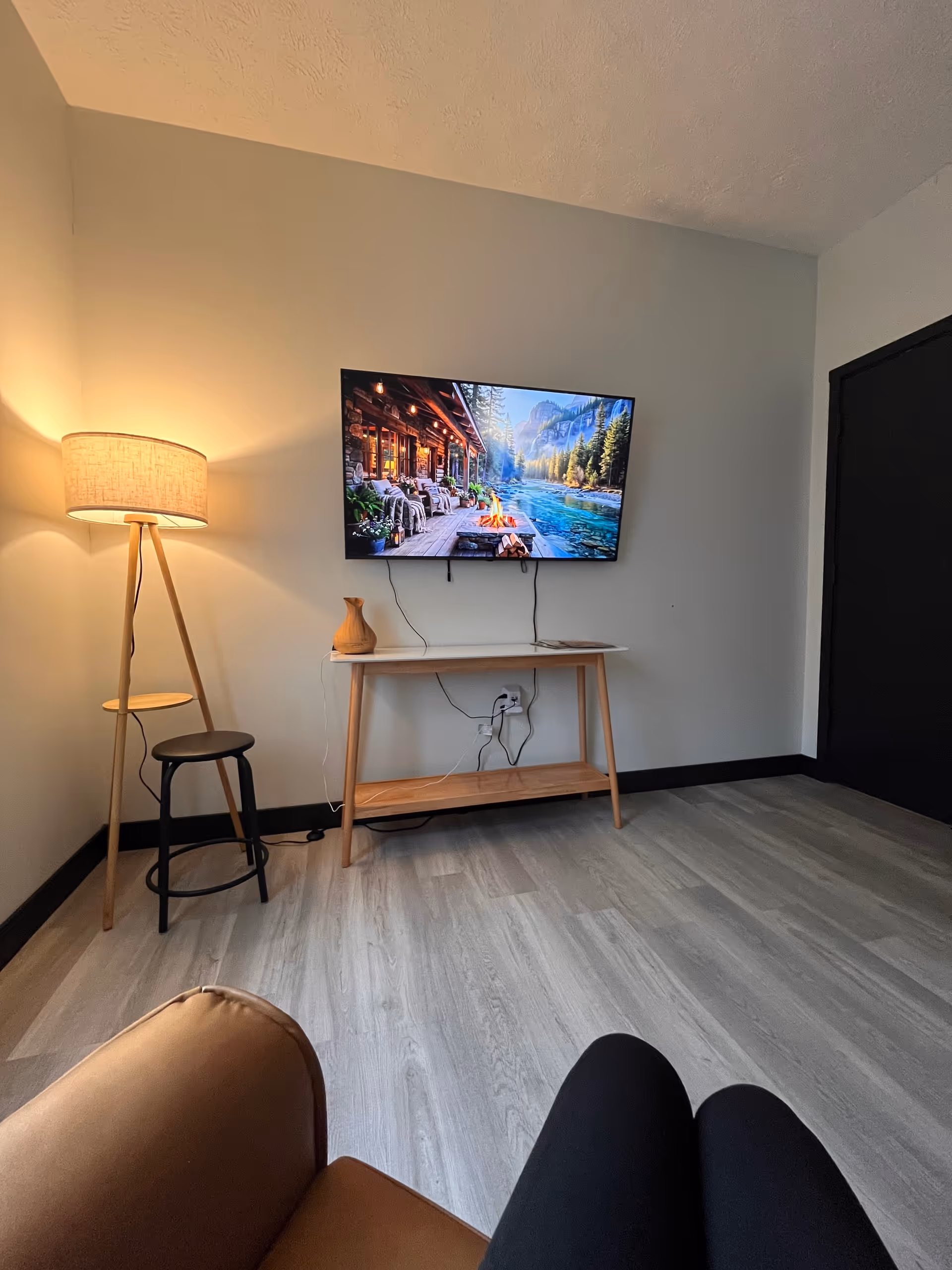 Living room setup with wall-mounted TV, console table, floor lamp, and visible legs of a person.
