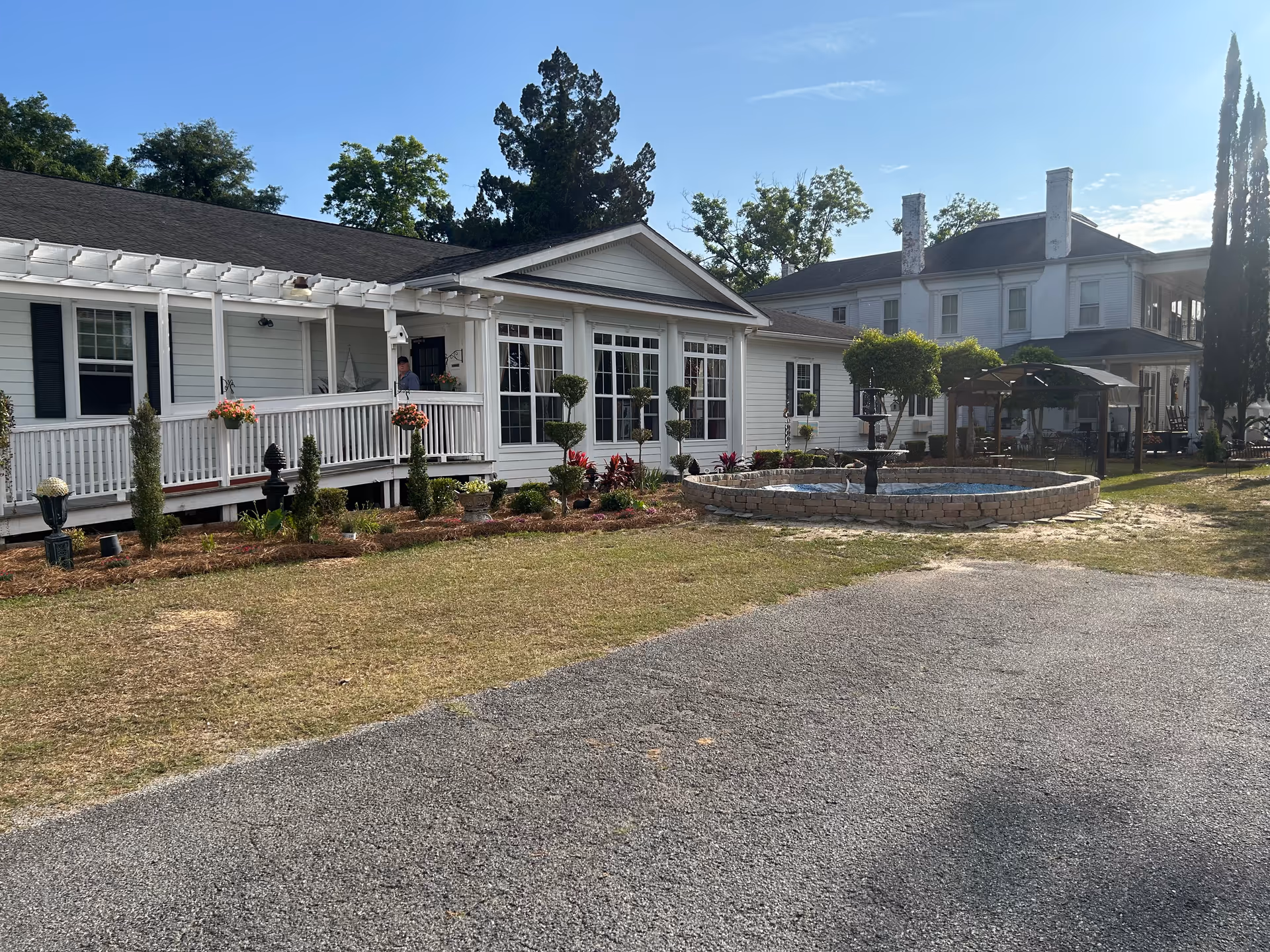 Exterior view of a white senior living facility with a circular stone fountain and patio.