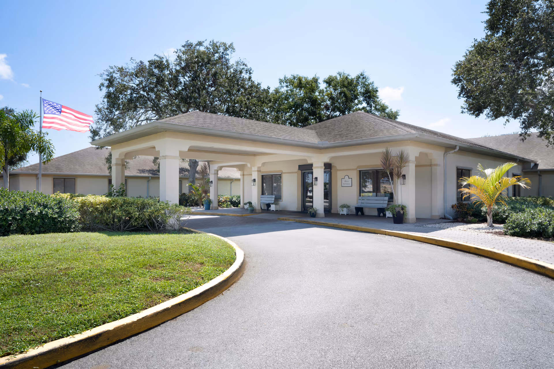 Front view of a senior living facility entrance with a curved driveway and flag.