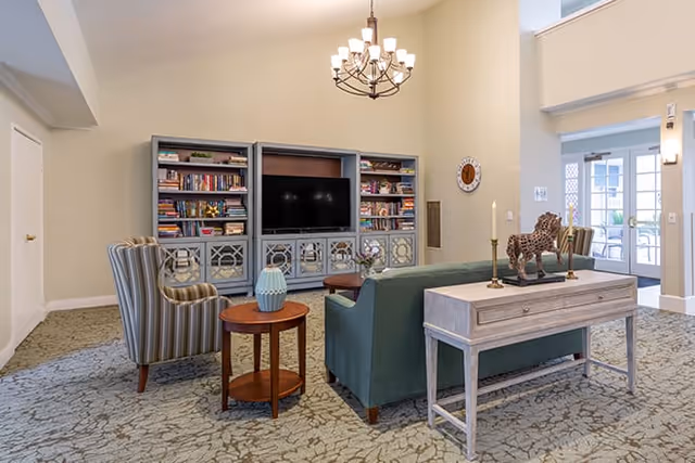 A spacious lounge with teal sofa, striped chair, built-in bookcase, TV, and chandelier.