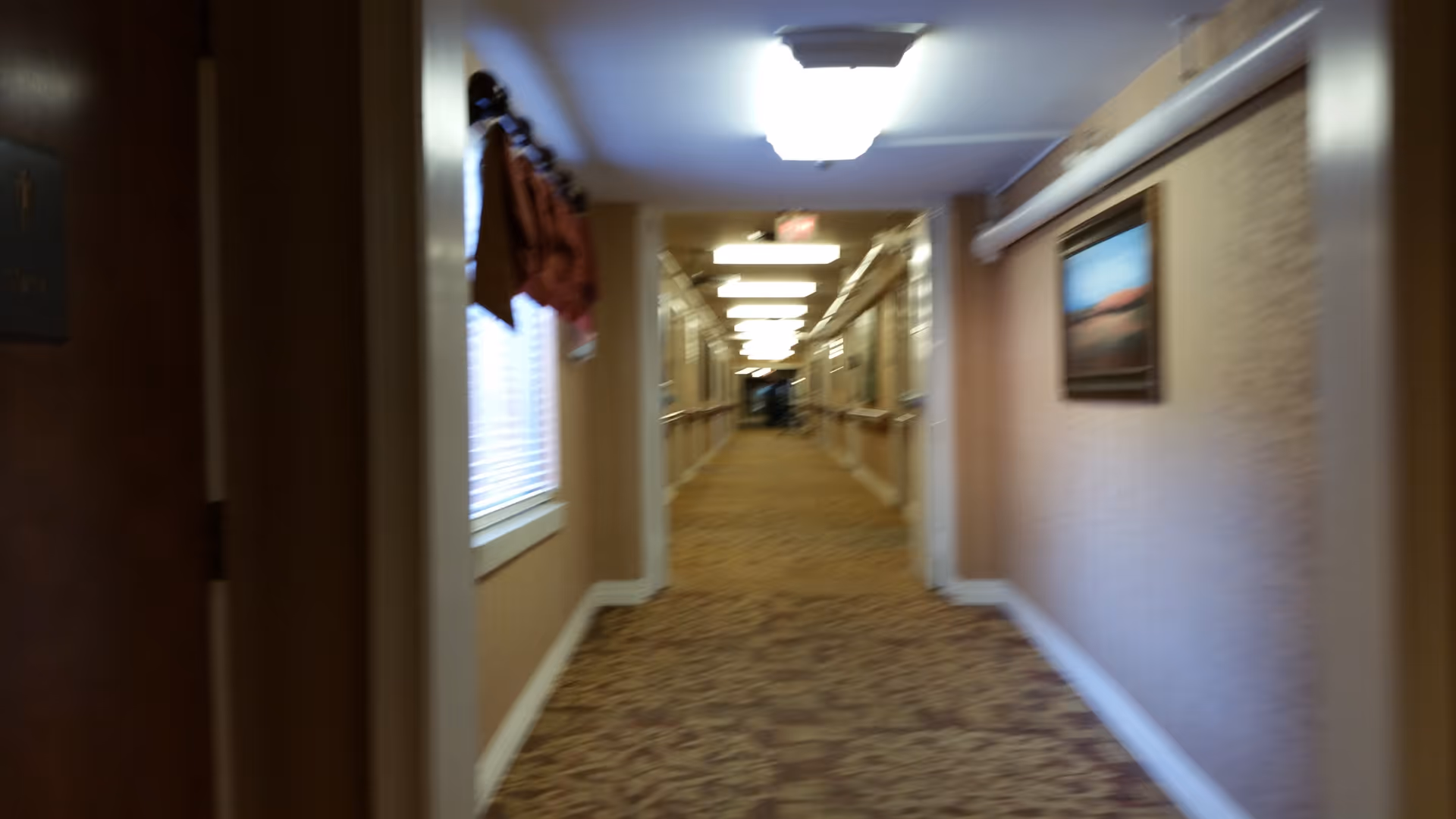 Long hallway in a senior living facility with coats on left and art on the right.