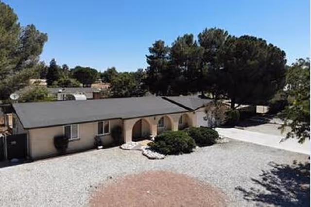 Exterior view of a single-story senior living building with gravel yard and trees.