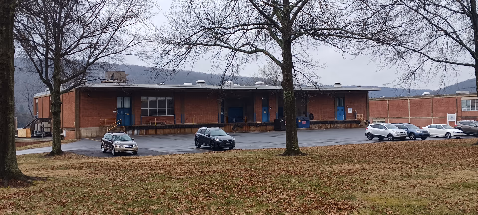 Brick single-story facility with blue doors, parked cars, and leaf-covered foreground.