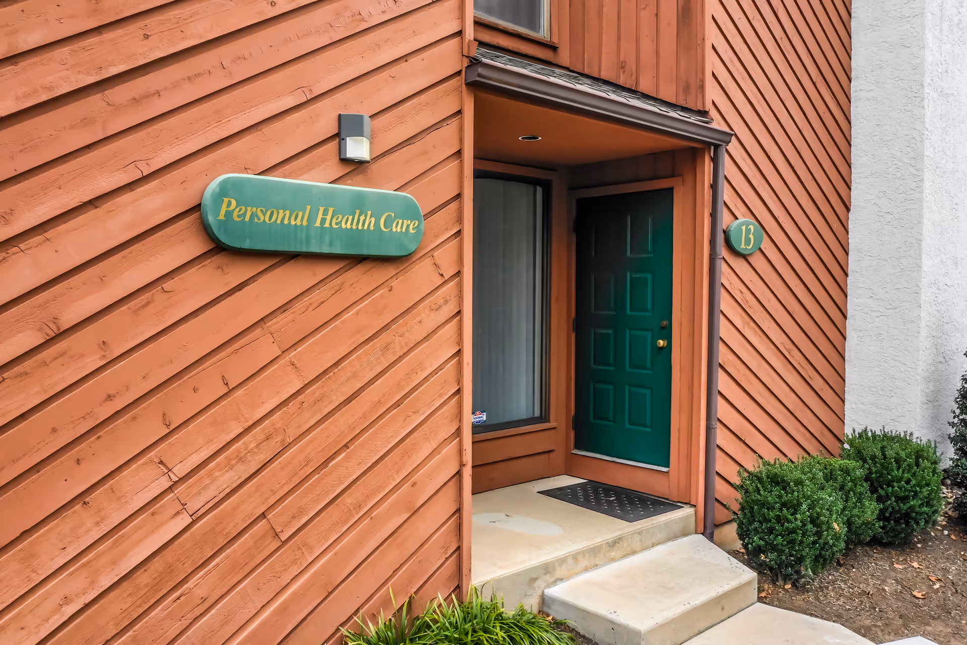 Wood-paneled exterior of a facility entrance with a green door and Personal Health Care sign.