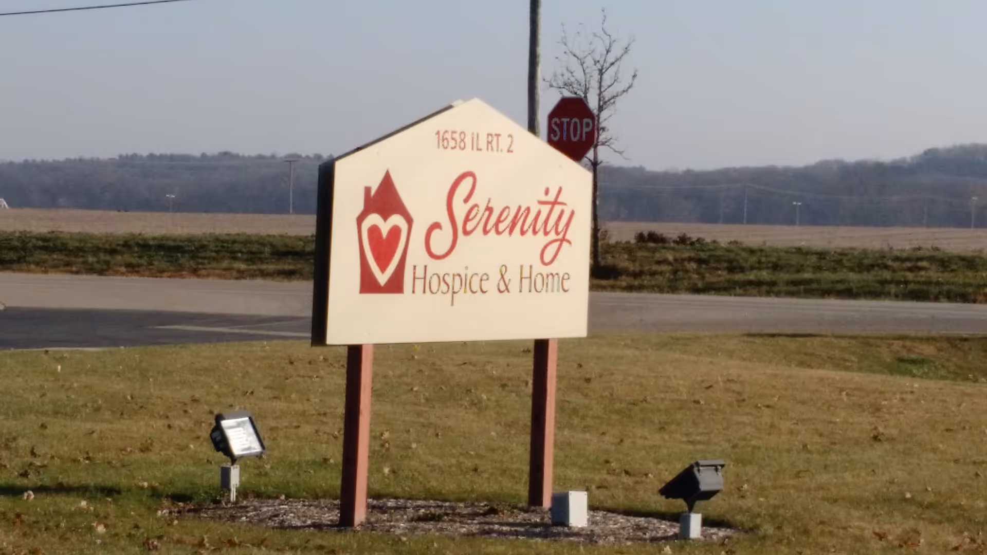 A Serenity Hospice & Home sign on a grassy roadside lot near the road.