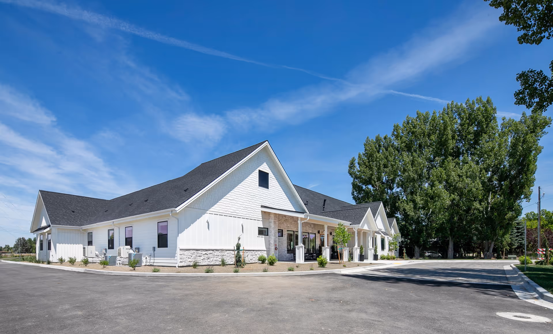 White single-story senior living facility with gabled roof, entry porch, and surrounding parking lot.