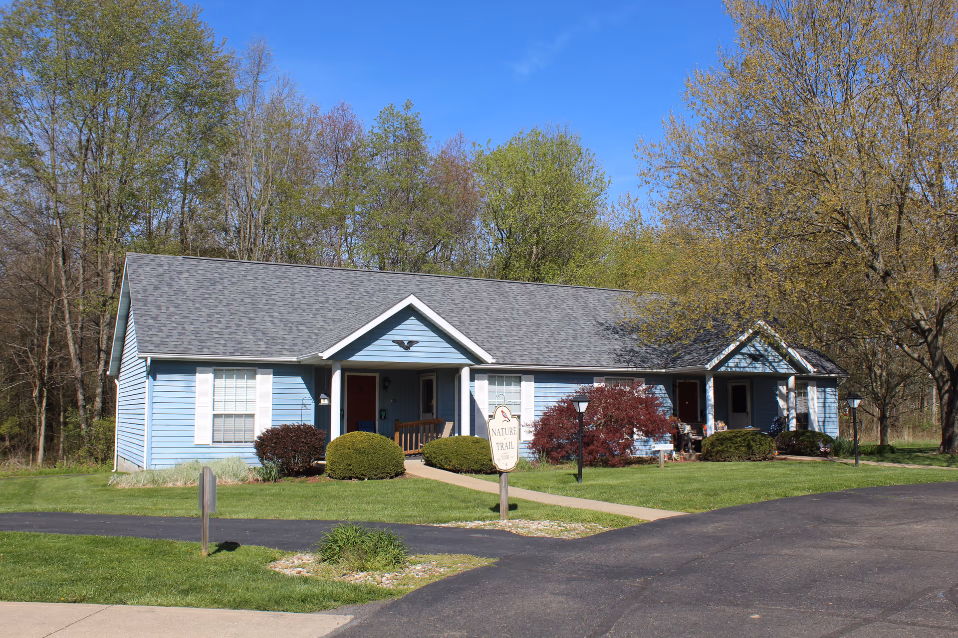 Single-story blue building with a front porch, landscaped lawn and trees in the background.
