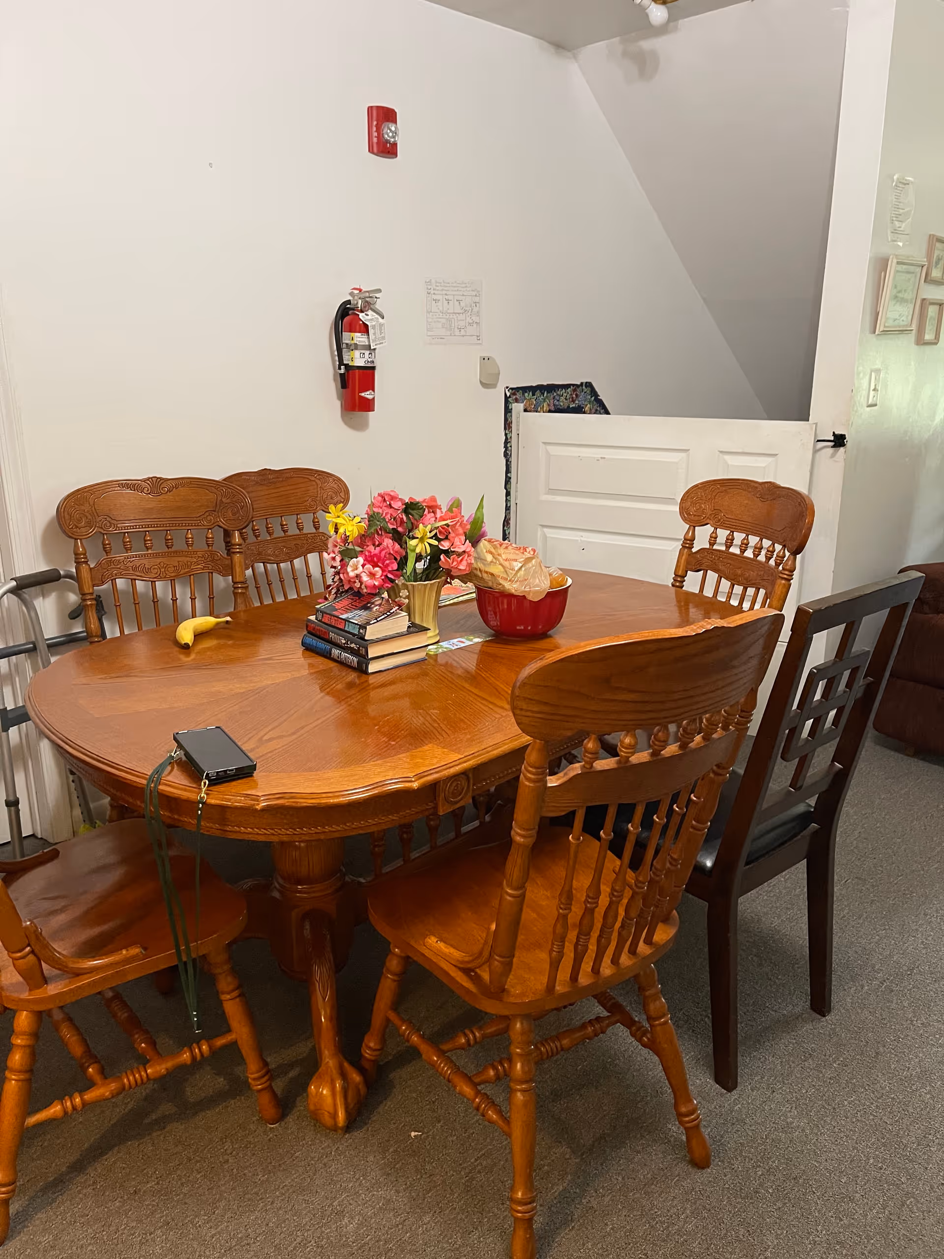 Round wooden dining table with chairs, flowers, and a red bowl in an indoor dining area.