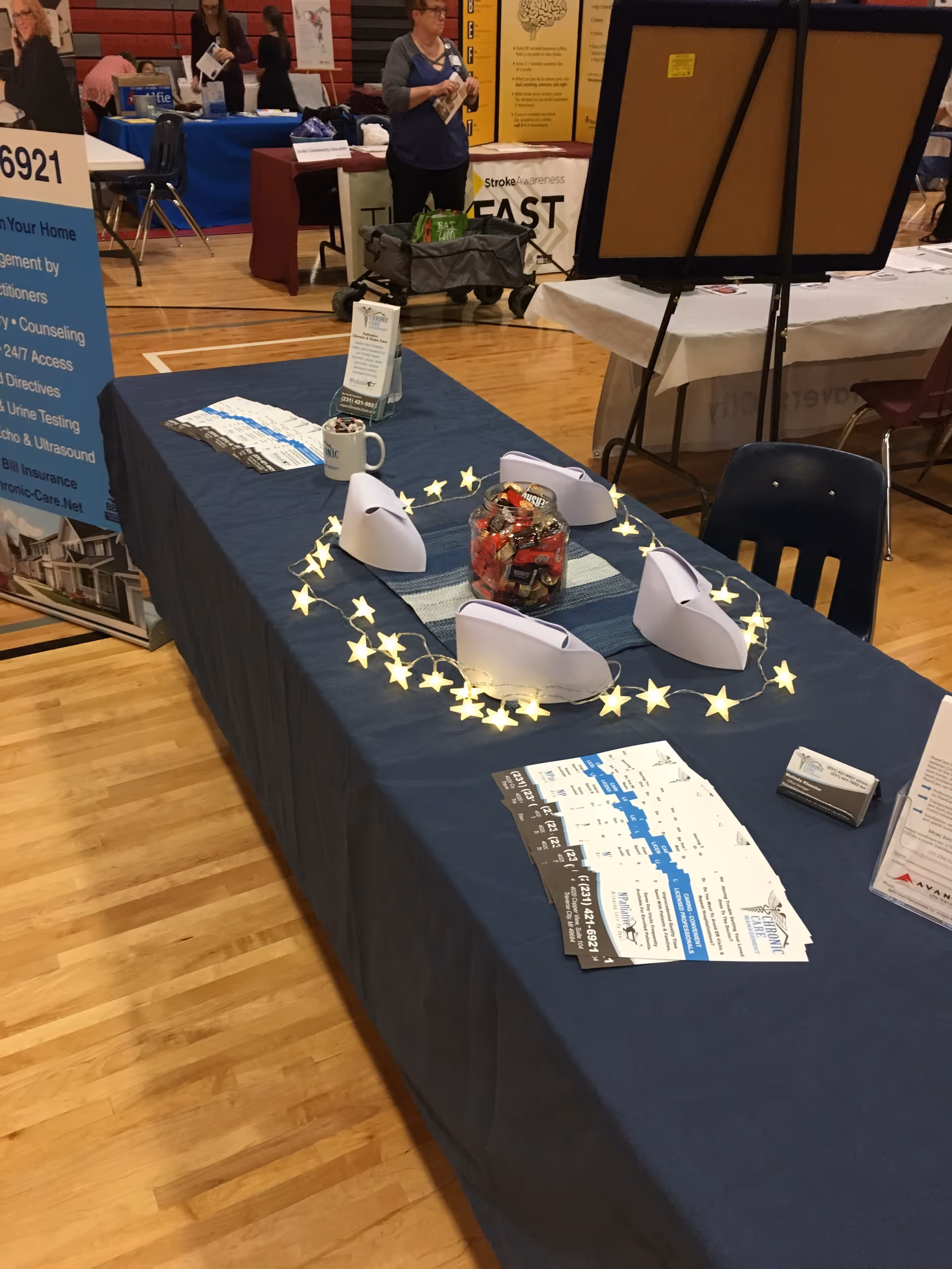 Exhibit table in a gym with brochures, garlands, and a candy jar.