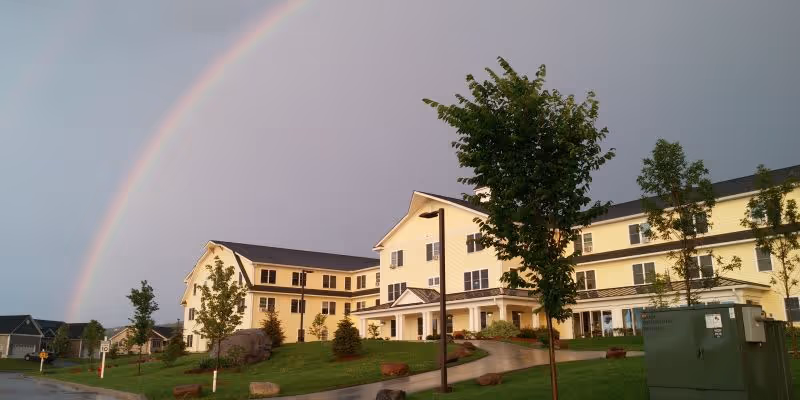 Yellow Homestead Senior Living building exterior with a rainbow arching over the entrance and landscaping.