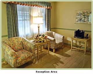Reception area with floral upholstered chairs, a small table with flowers, lamp, and windows.