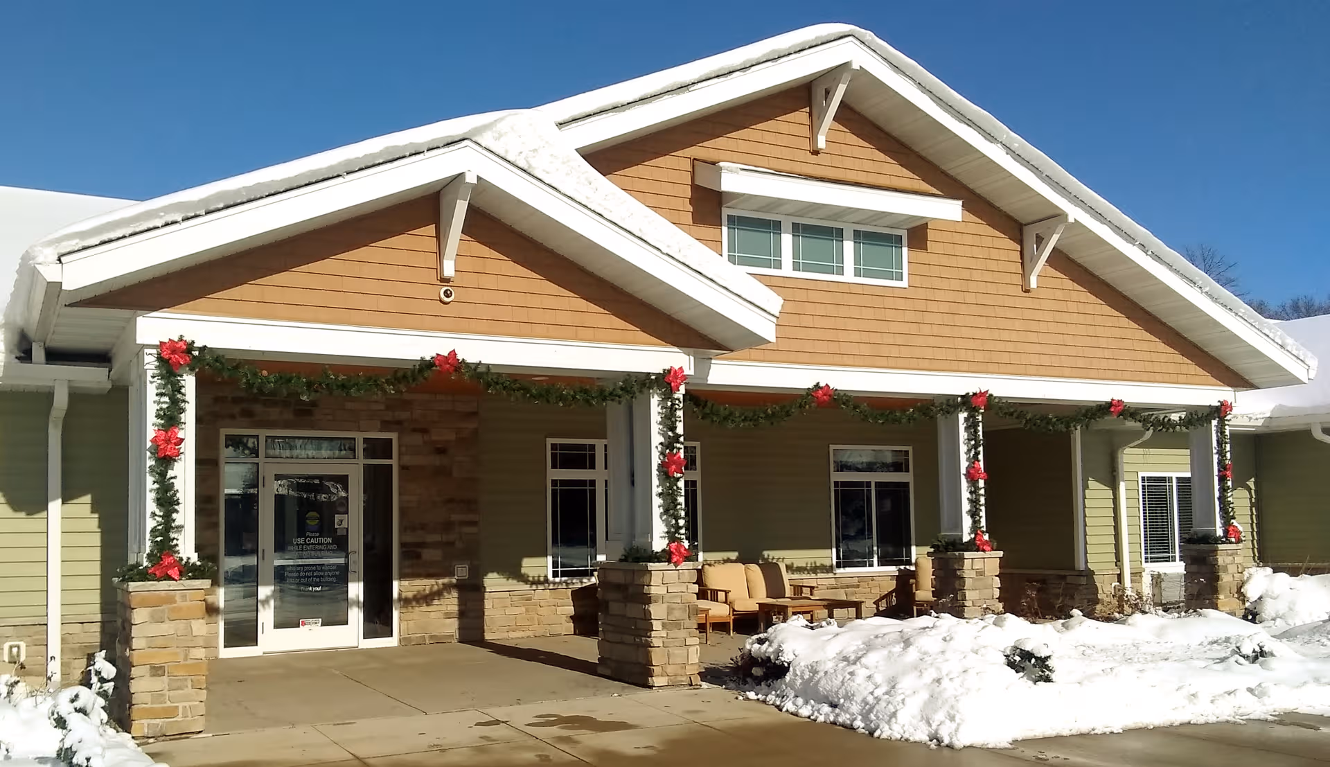 Front exterior of memory care facility with snow, decorated porch, and seating.