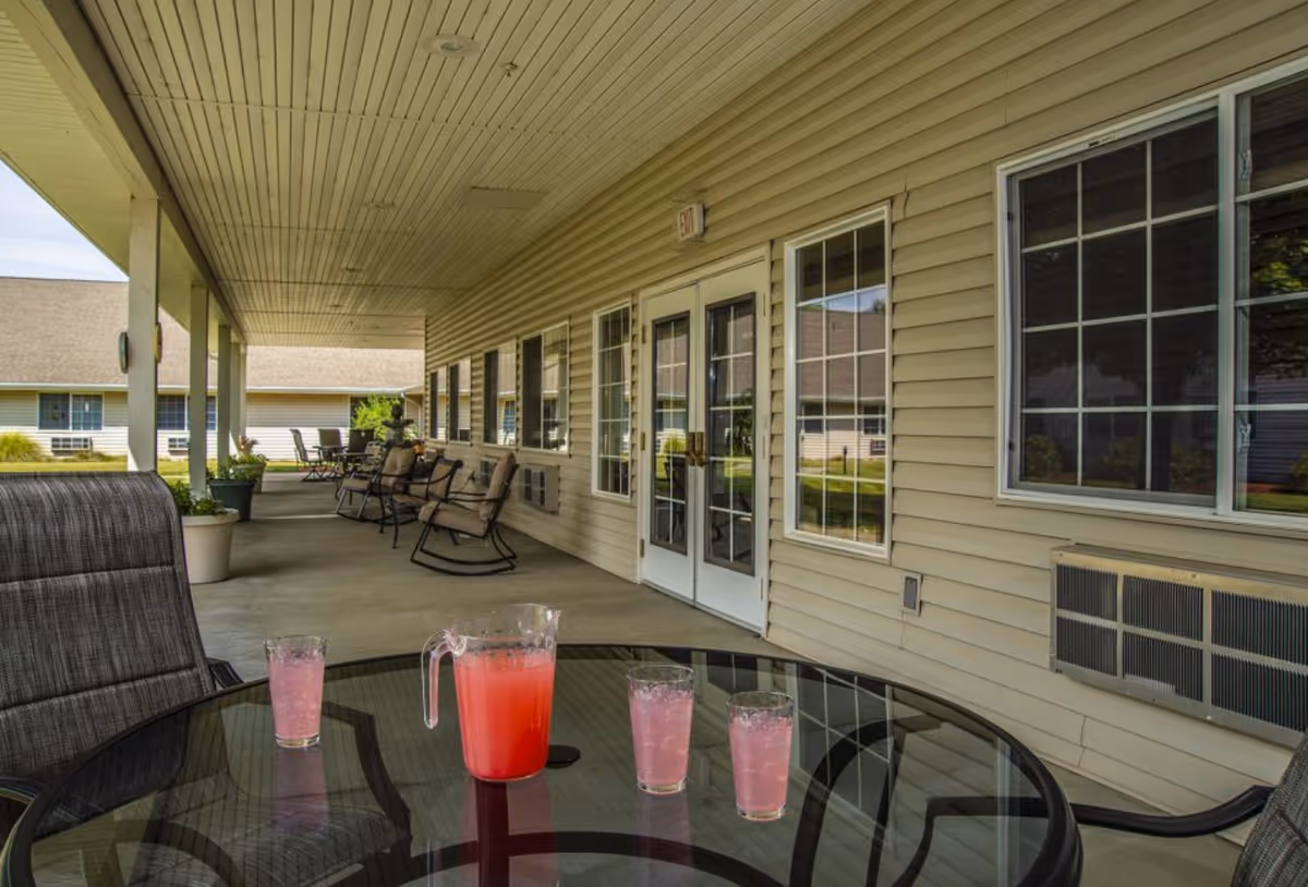 Covered outdoor patio at Apple Springs Senior Living with glass table, pink pitcher, and chairs.