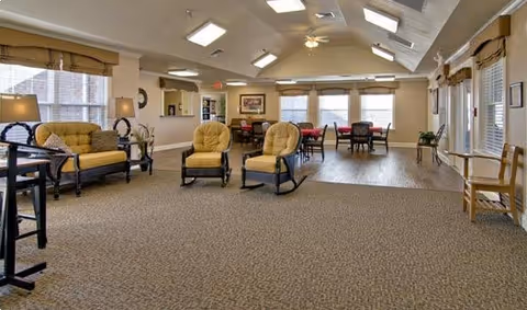 Spacious senior living common area with beige upholstered seating, tables, and large windows.