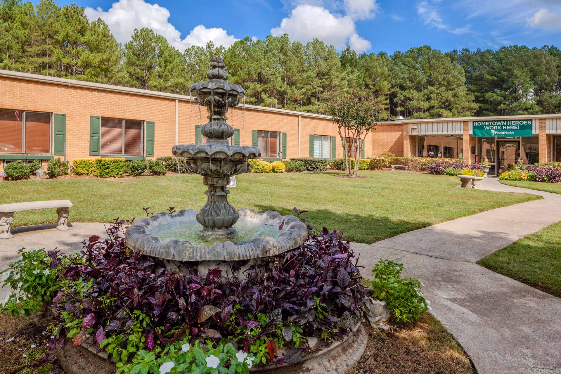 Brick senior living facility exterior with a central fountain and landscaped grounds.