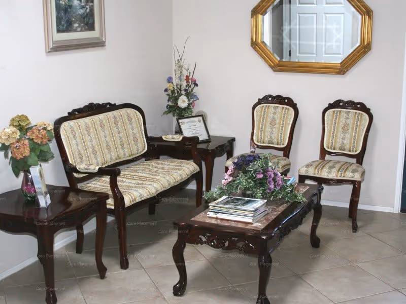 A formal waiting area with wooden-framed upholstered chairs, a coffee table, and floral decor.