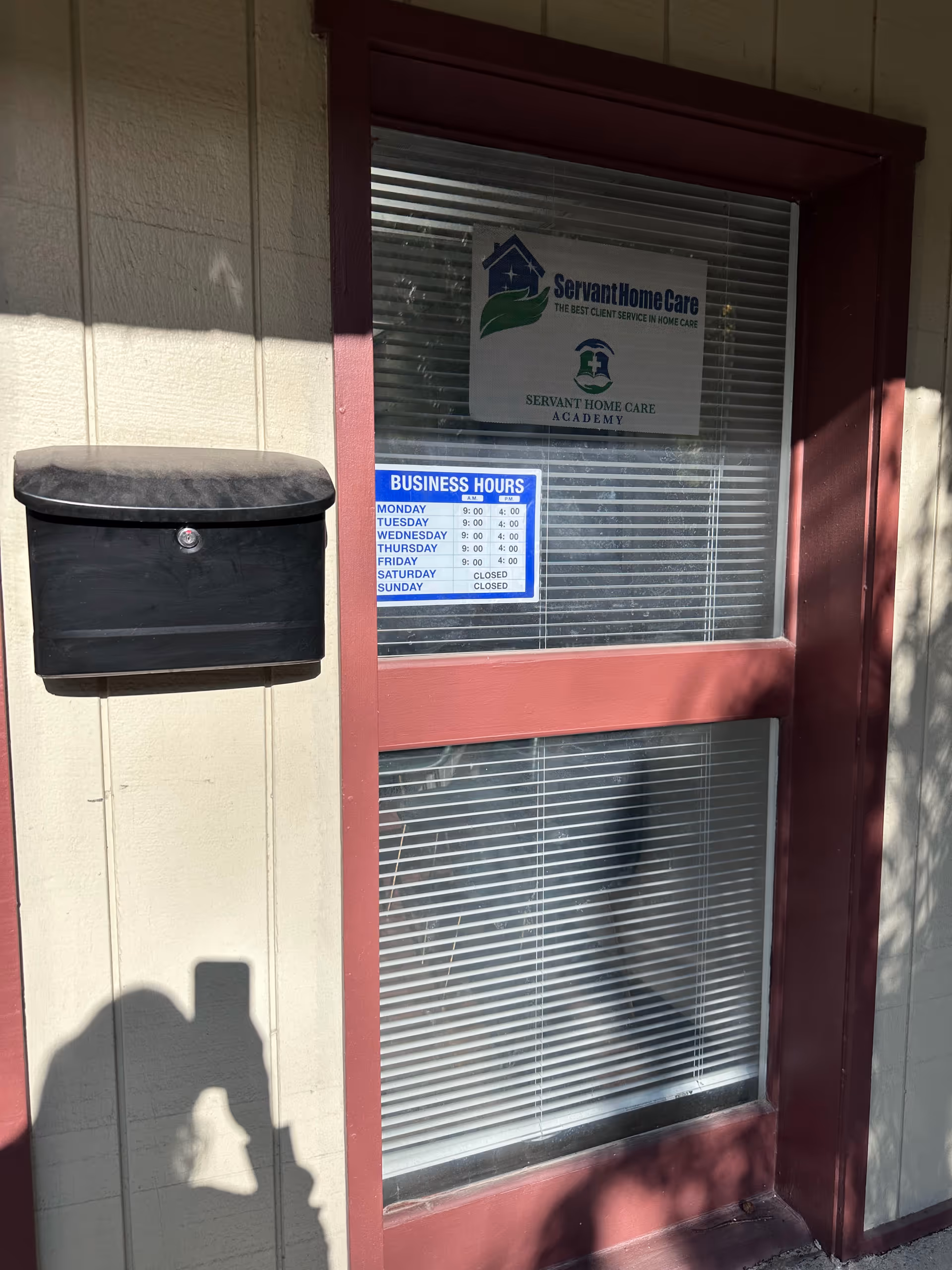 Exterior wall with a red-framed window, black mailbox, and Servant Home Care signs.