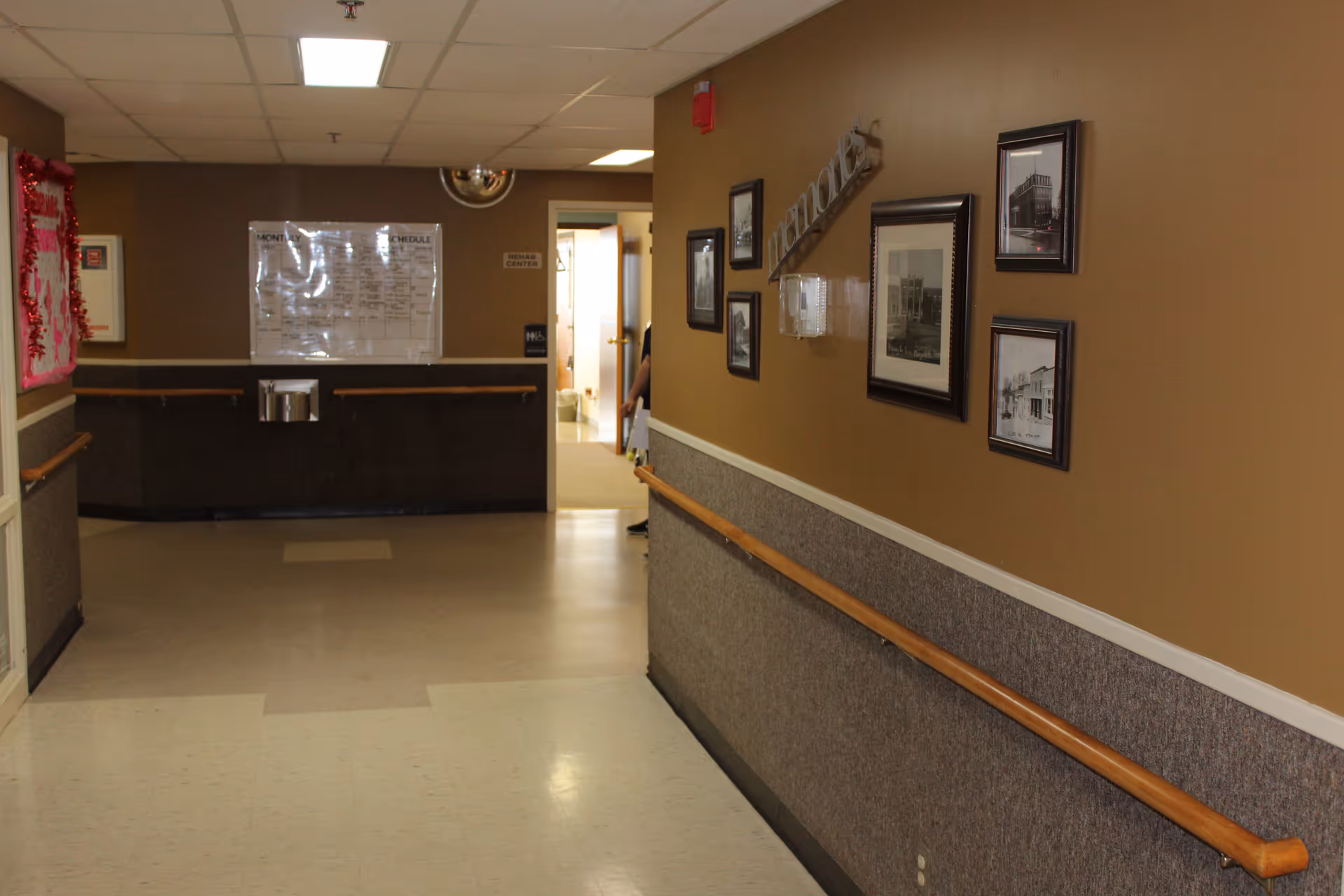Long interior hallway of Nodaway Nursing Home with framed photos and a front desk.