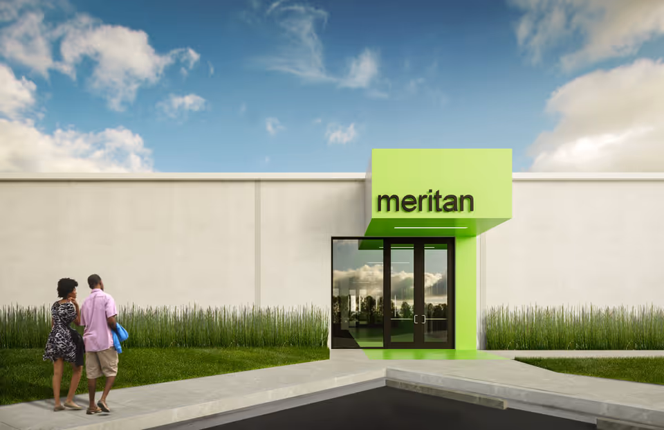 Modern facility entrance with bright green sign reading meritan, glass doors, and two pedestrians outside.