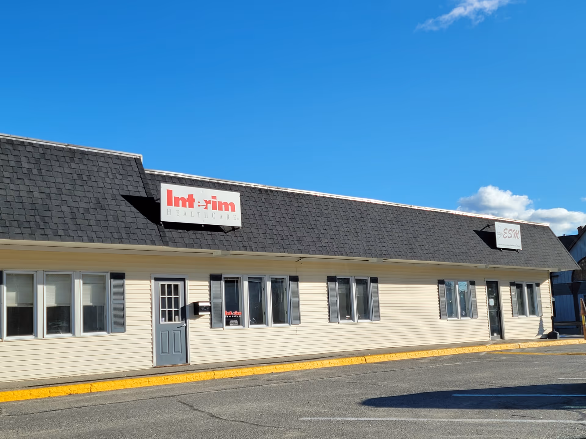Front view of a beige, single-story building with a dark roof and Interim HealthCare sign.