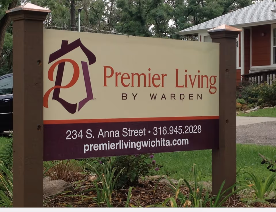 A large beige sign reads Premier Living by Warden with a house behind.