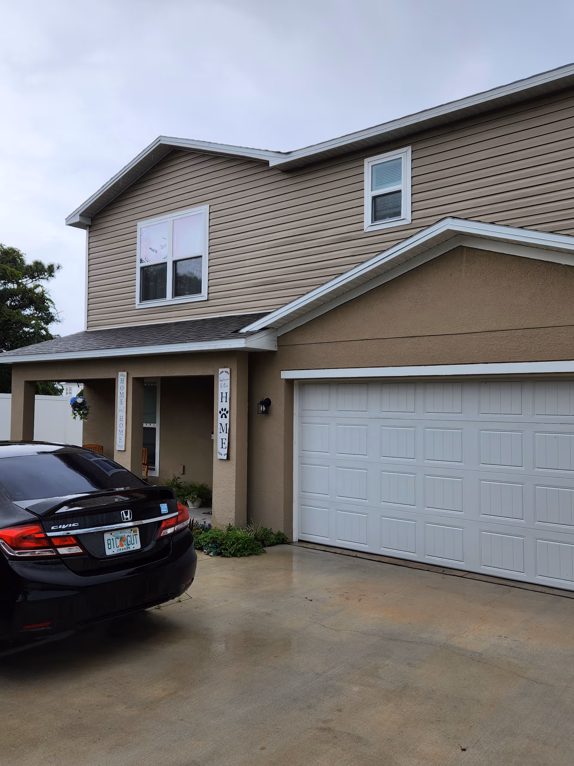 Two-story beige senior living home with garage, driveway, and welcome signs.