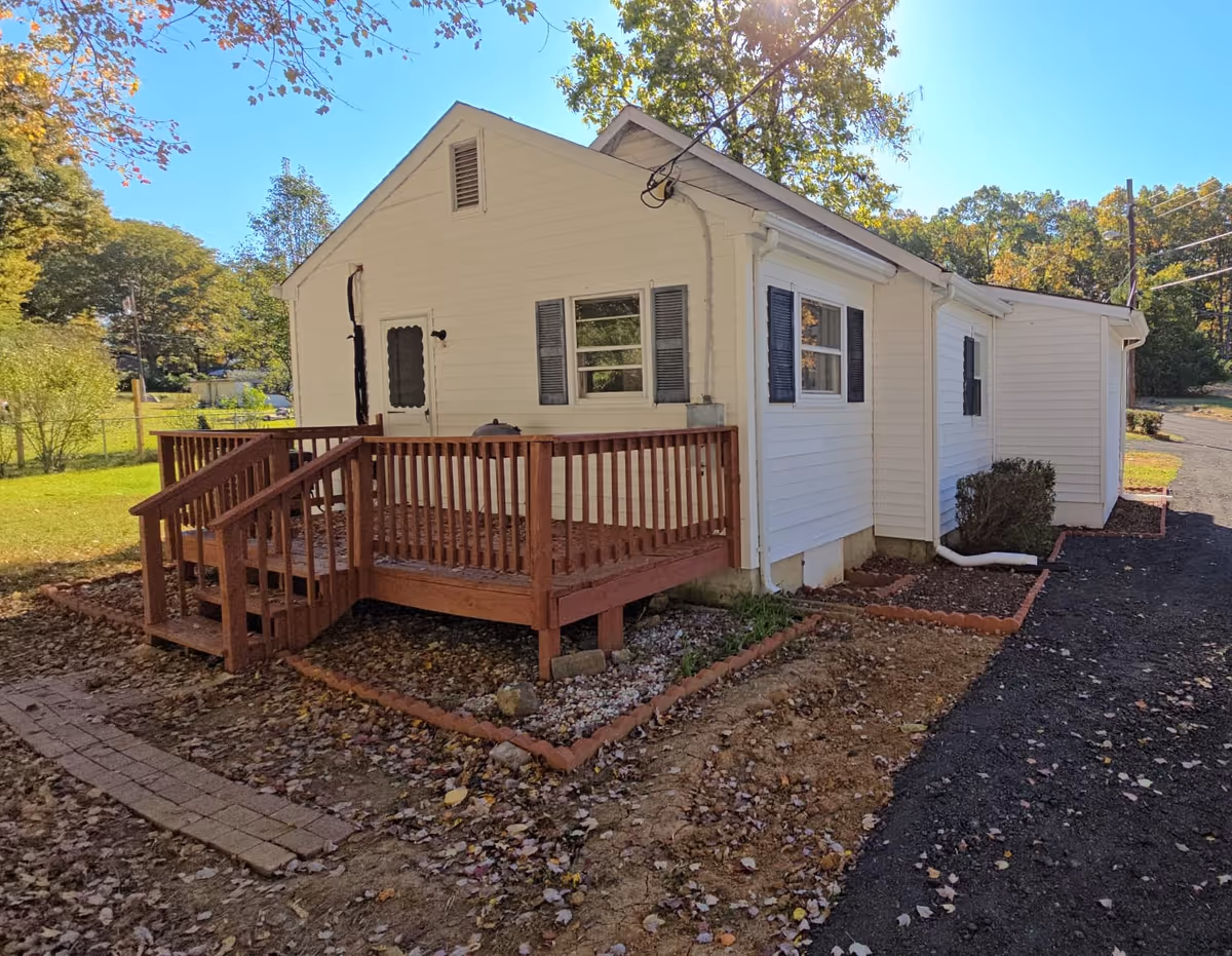 White single-story building with a wooden deck and surrounding yard.