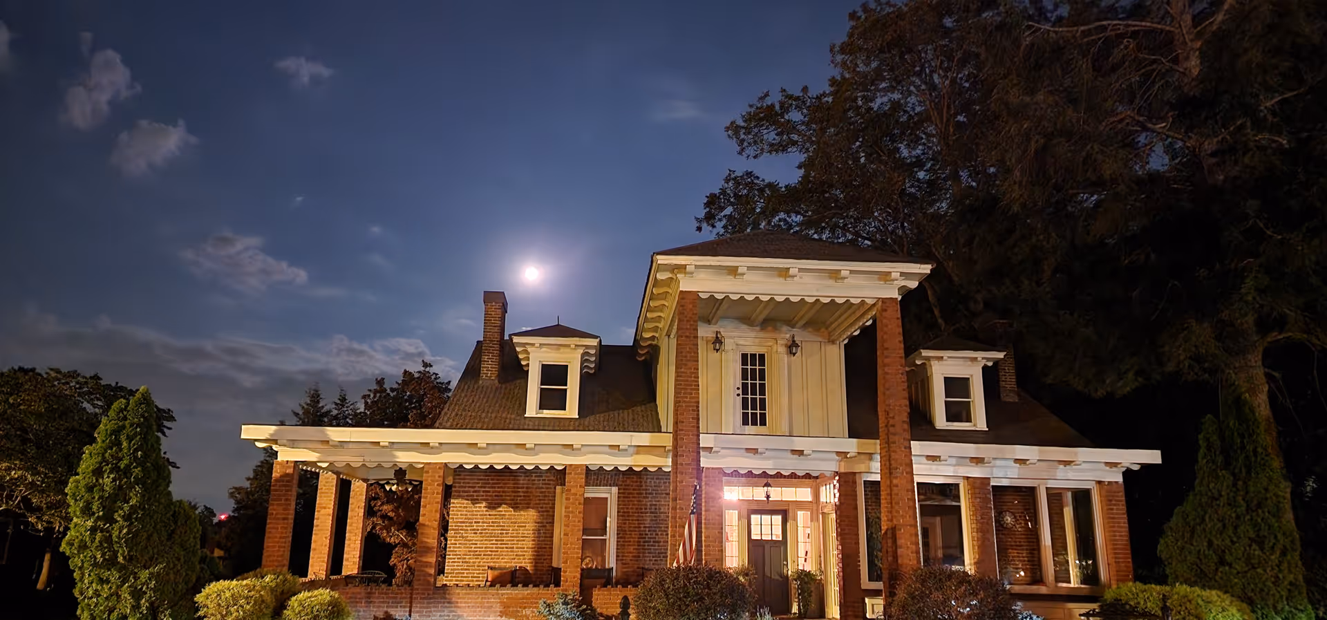 Nighttime exterior of a brick building with columns and a lit front entrance.