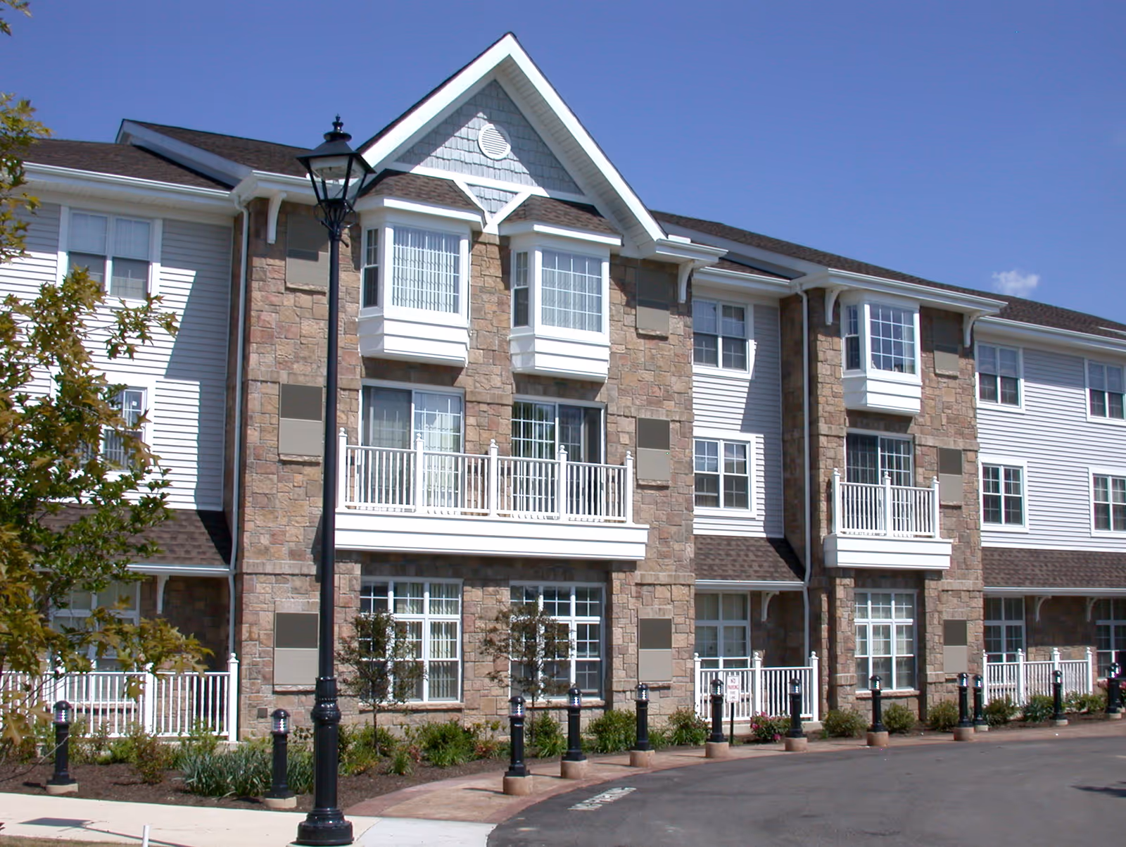 Three-story retirement community building with stone facade, white balconies, and a street lamp.