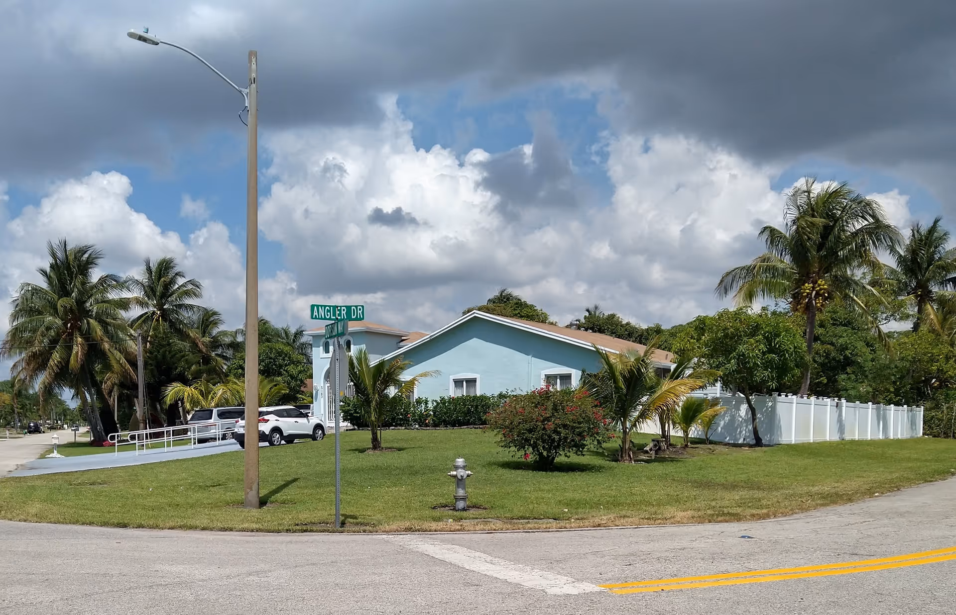 Exterior view of a light-blue, single-story assisted living building with palm trees and a white fence.