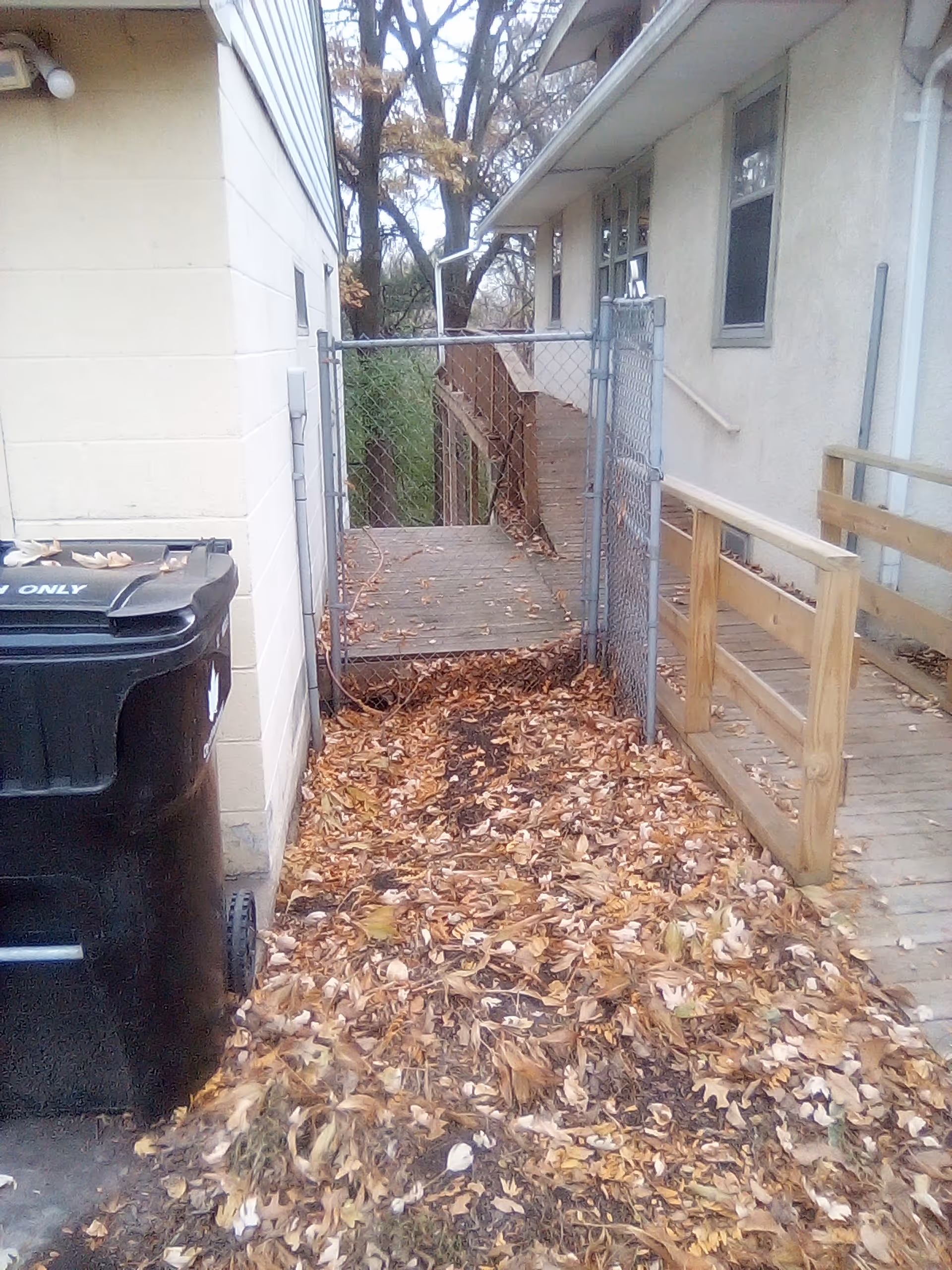 An outdoor walkway between buildings with a gate, wooden railing, and autumn leaves.