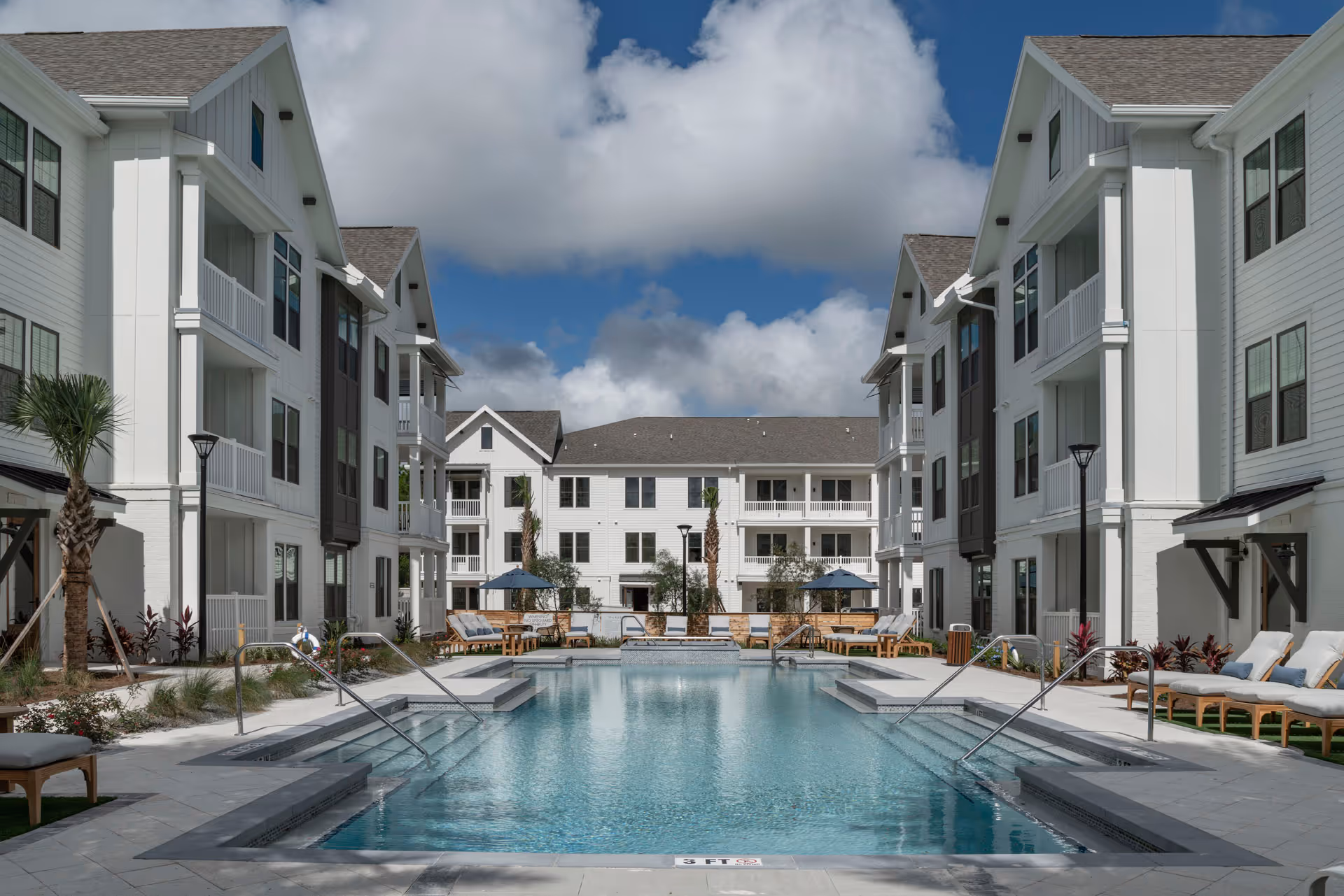 Outdoor pool surrounded by white, multi-story senior living buildings with lounge chairs.