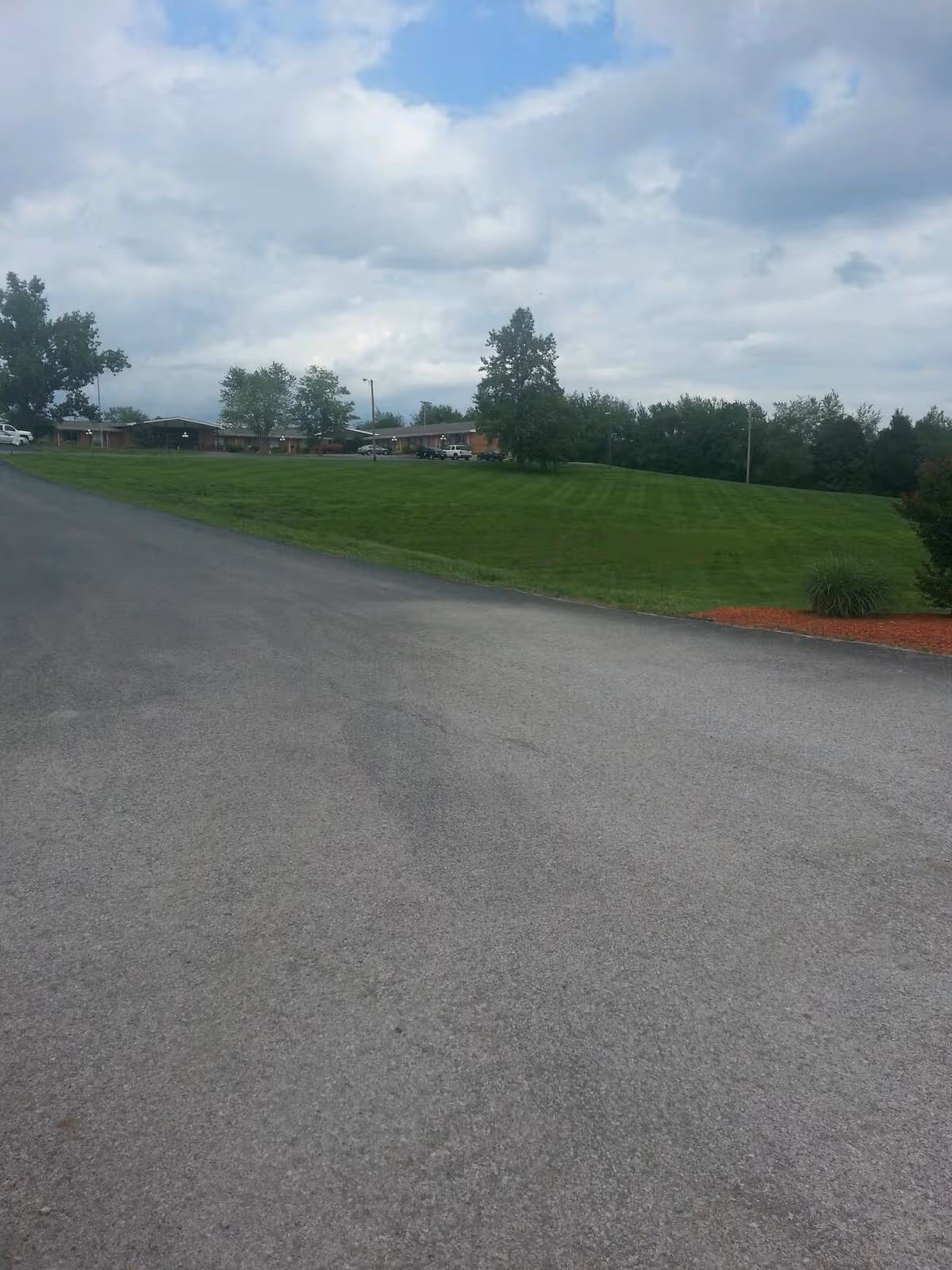Wide exterior view of a road leading to a senior living campus with green lawn.