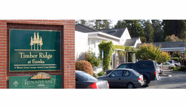 Timber Ridge at Eureka sign on brick wall with building front and parked cars.