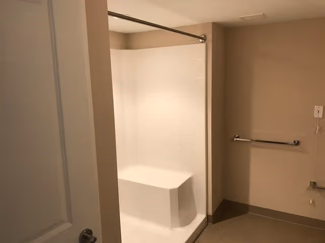 A bathroom with a white shower area featuring a built-in seat, beige walls, a towel bar, and a partially open door with a silver handle.