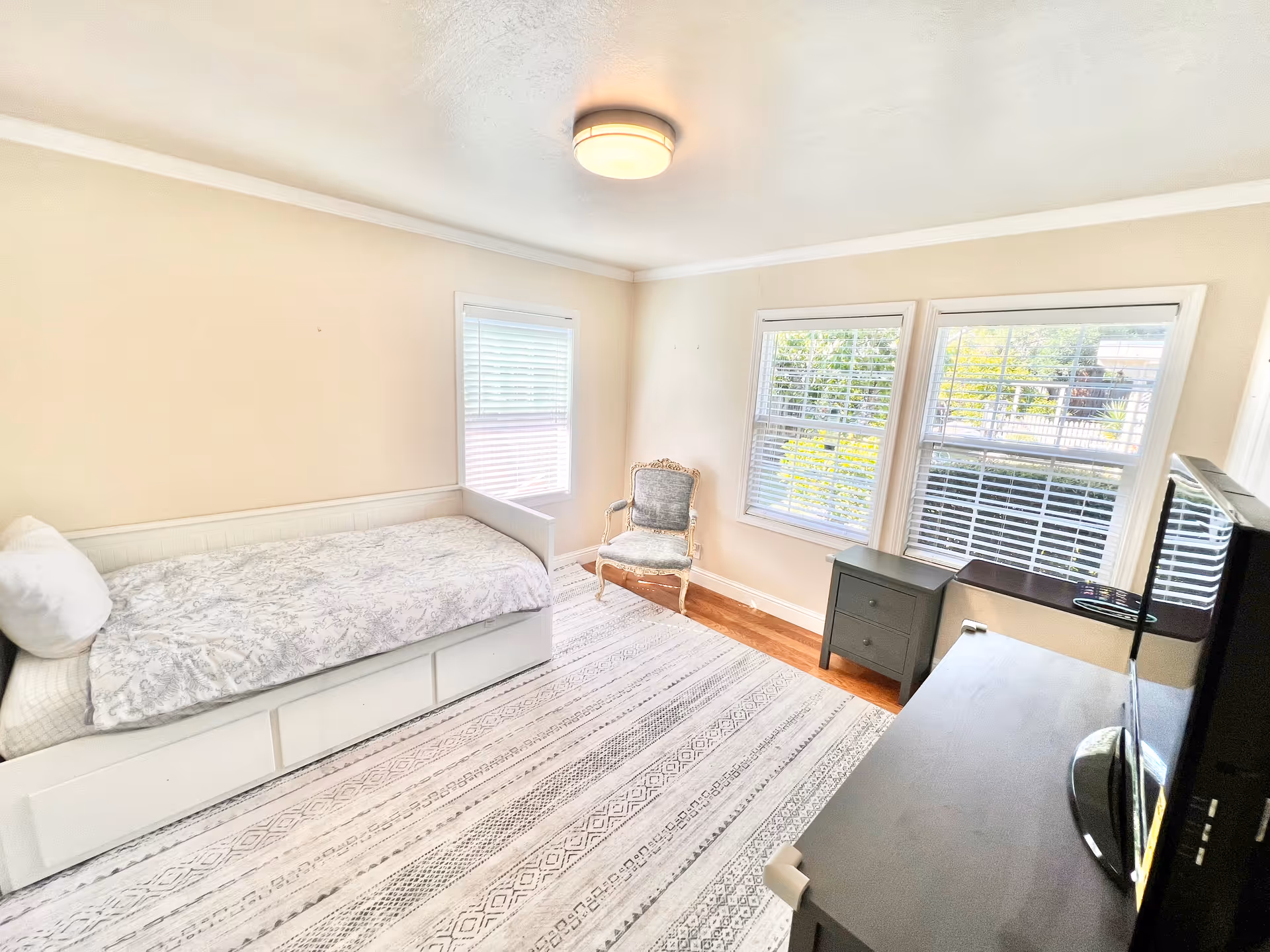 Bright bedroom with a single bed, windows, chair, and dresser in a clean space.