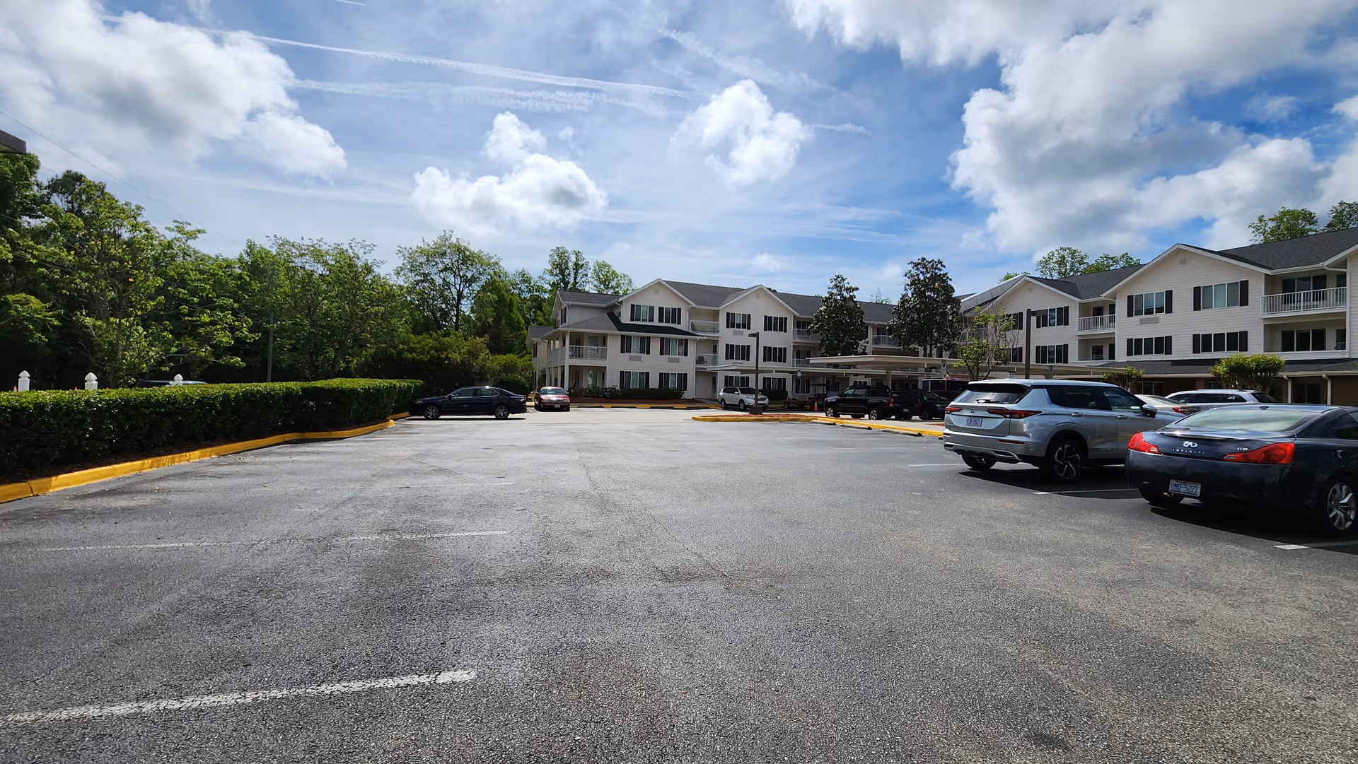 Wide parking lot in front of a multi-wing senior living building with trees and cars.