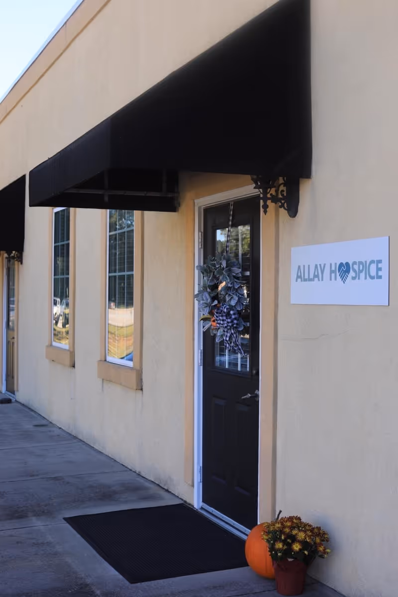 Front entrance of Allay Hospice building with wreath, sign, awning, and pumpkin decoration.
