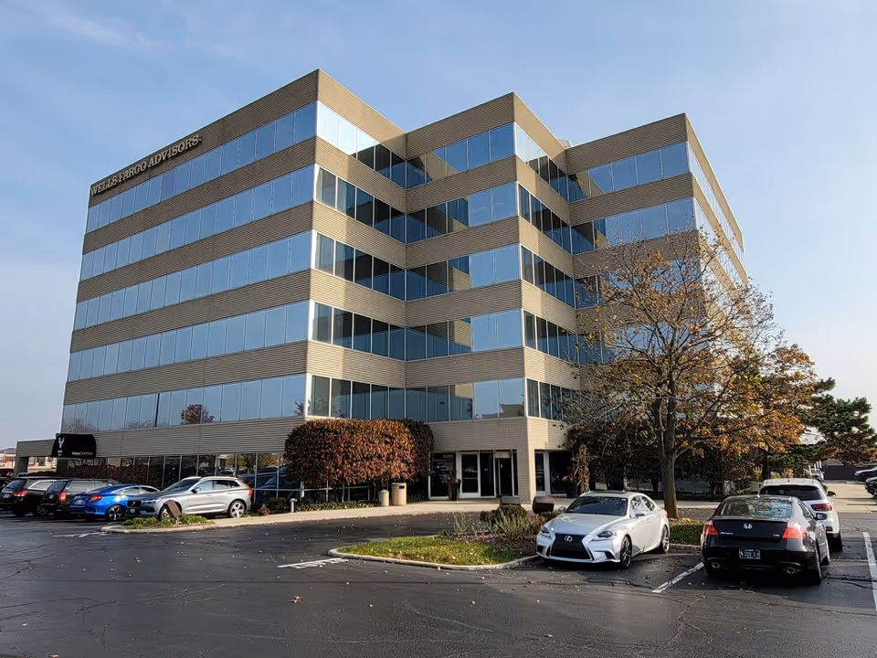 Modern glass-front building with multiple stories and a front parking lot.