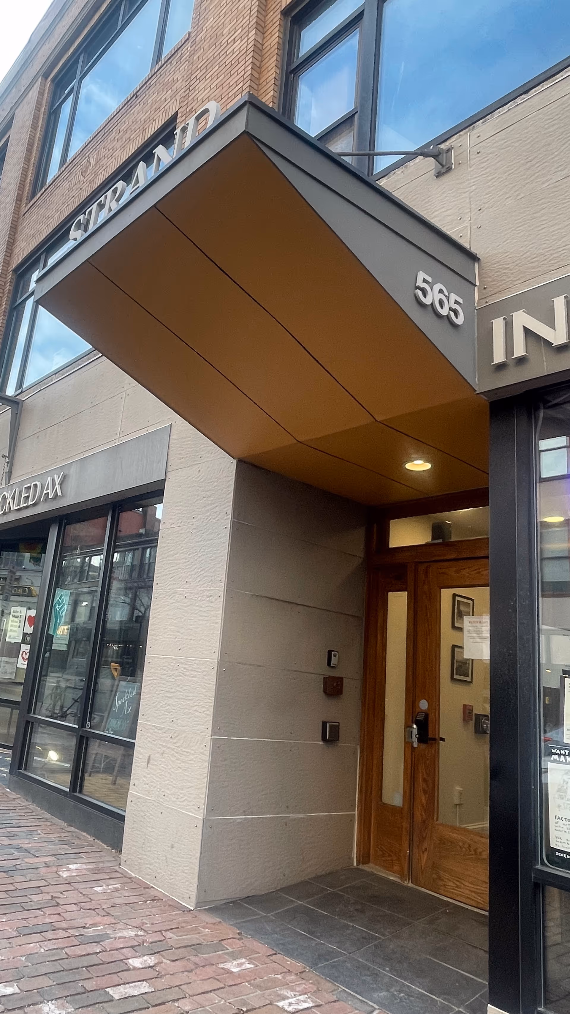 Exterior storefront entrance with a brown wooden door under a brown metal canopy.