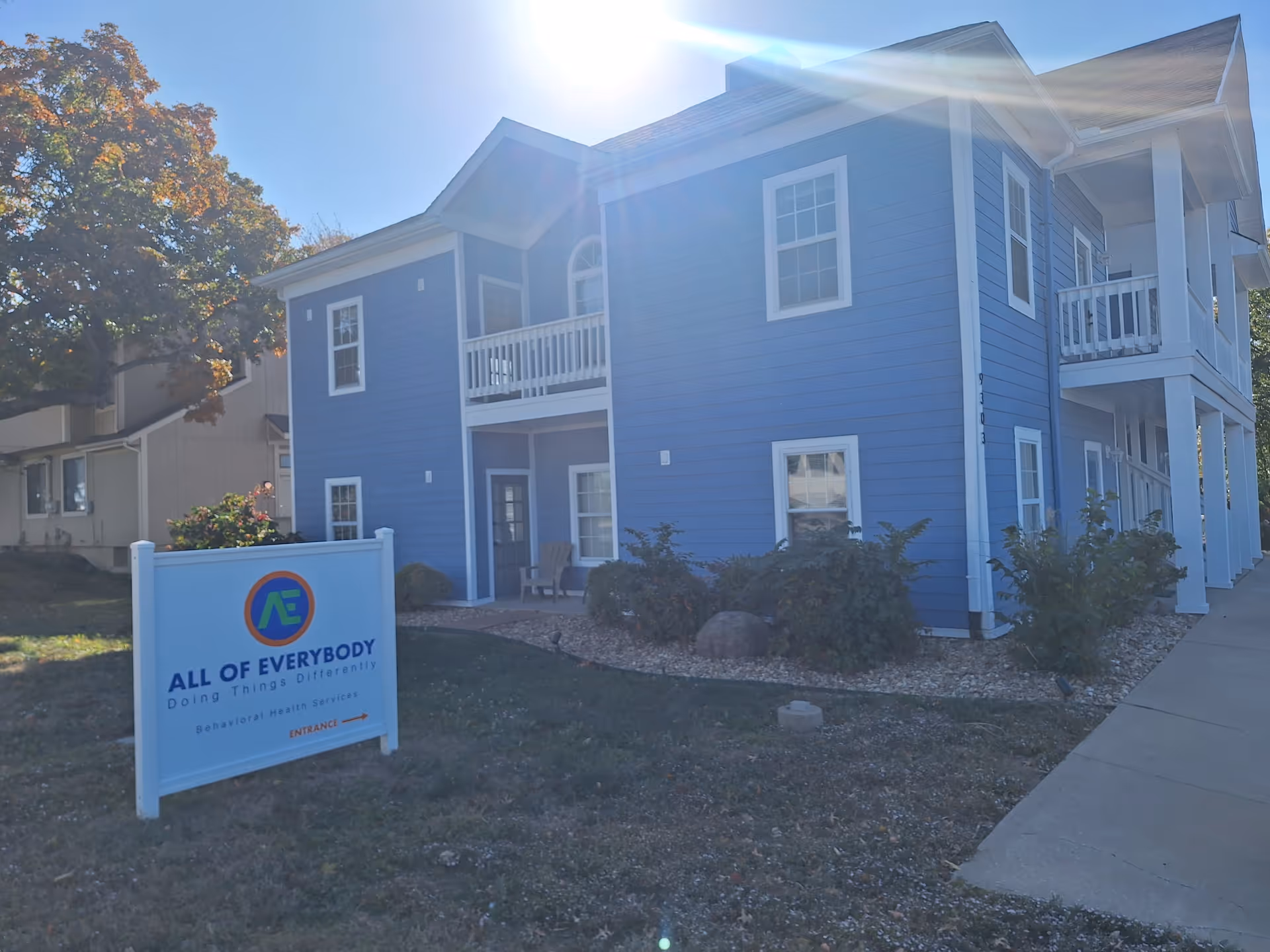 Blue two-story senior living building with a sign reading All of Everybody in the front yard.