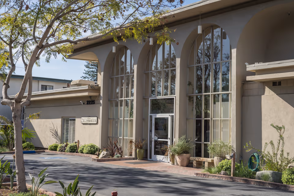 The Californian facility's front entrance with large arched windows and potted plants.