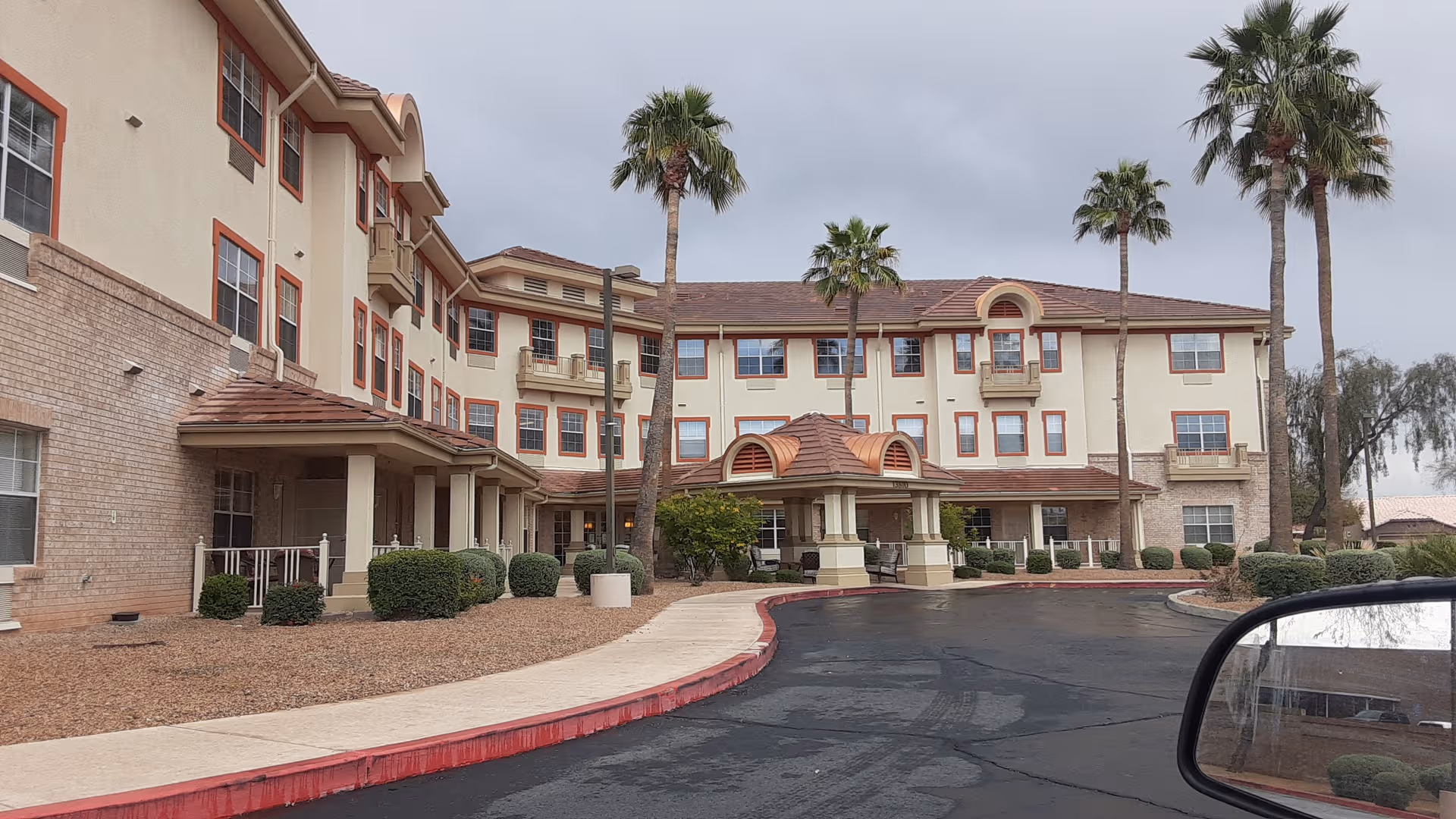 Exterior view of Sun City West Assisted Living with curved driveway and palm trees