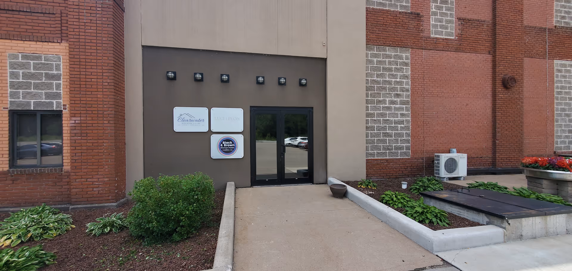 Exterior view of Clearwater Assisted Living entrance with brick walls, glass doors and landscaping.