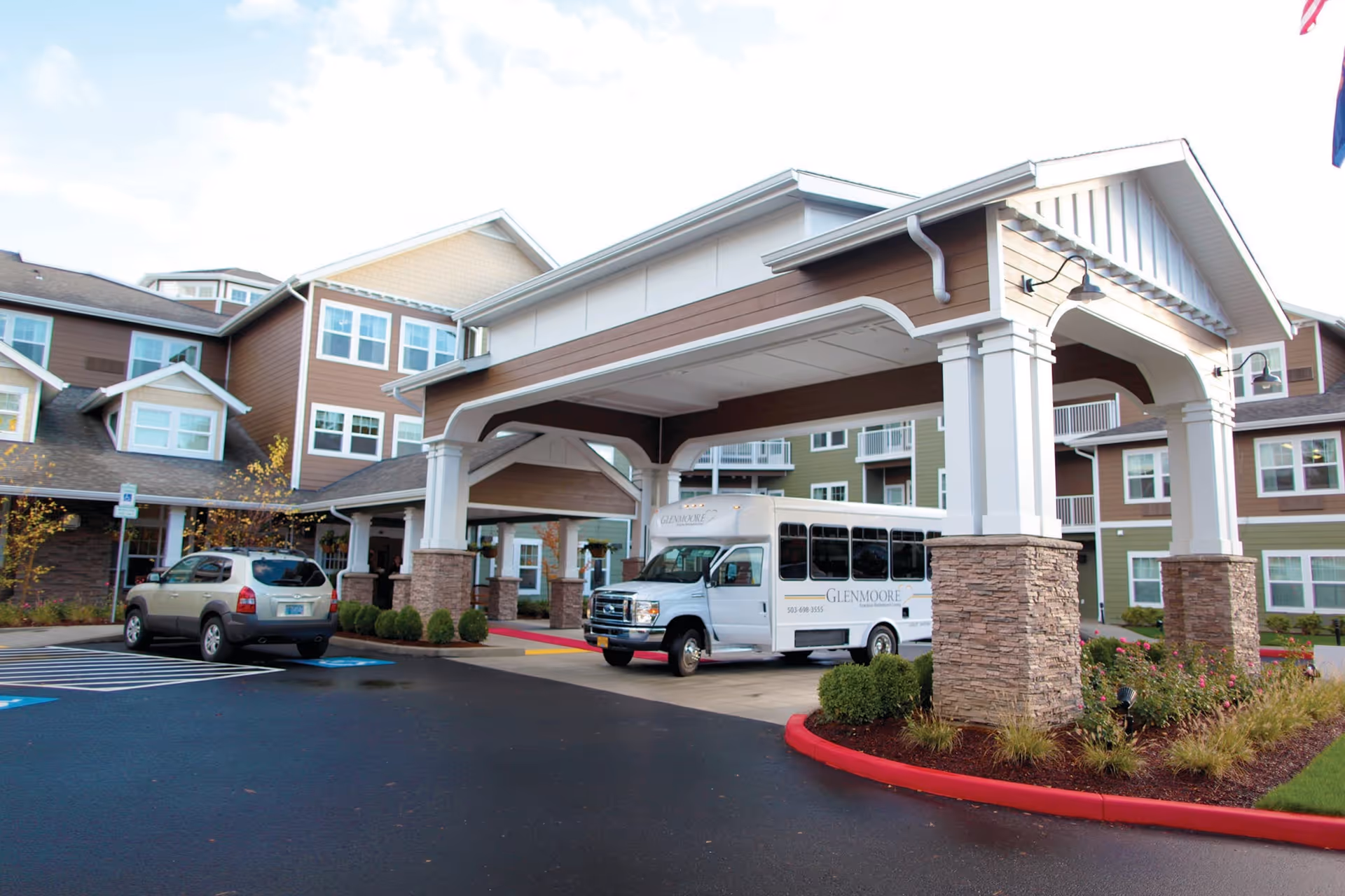 Front view of a senior living facility entrance with a bus and landscaped drop-off area.