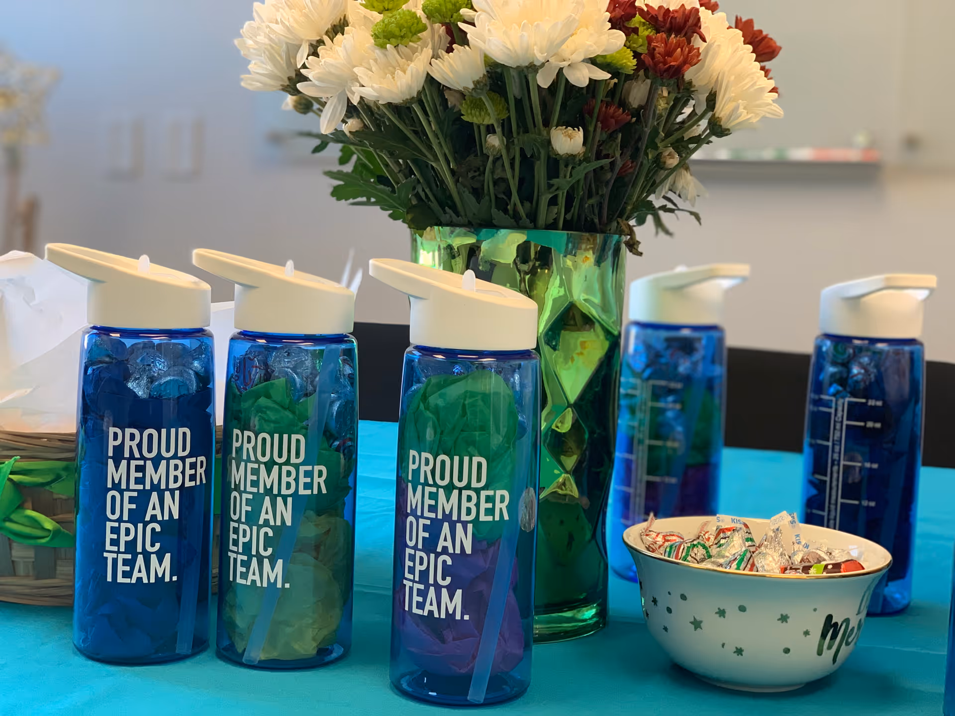 Indoor table with blue water bottles, a green vase of white flowers, and a candy bowl.